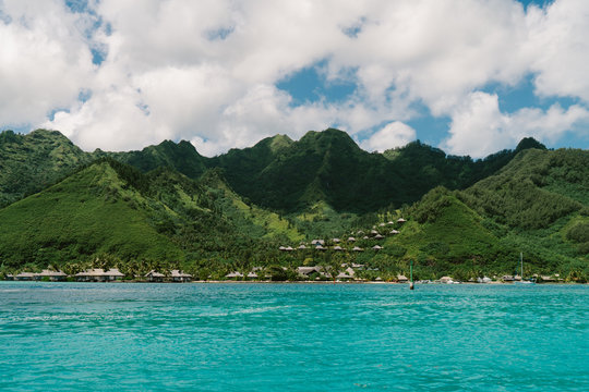 Green mountains, sea, cloudy sky and bungalows, Tahiti, South Pacific