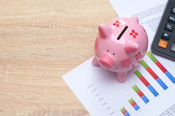 Pink piggy bank with graph and calculator on wooden desk - growing interest rate concept.