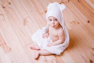 baby boy with brown eyes is five months old wrapped in a white towel with ears on wooden background .