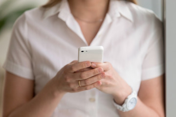 Close up photo of trendy cellphone in womans hands. Female holding modern white phone and dialing number or typing a message. Office worker entertains with mobile apps, using mobile banking service