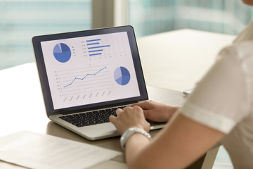 Businesswoman at desk analyzing statistic data on laptop screen. Female entrepreneur examines company financial results on computer. Woman making business presentation with graphs, stats and diagrams