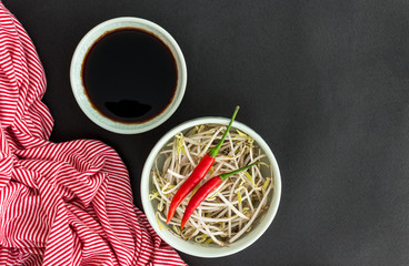 Obraz na płótnie Canvas Red chili peppers on soybean sprouts, soy sauce in bowl and a striped towel on black background. Asian food concept.