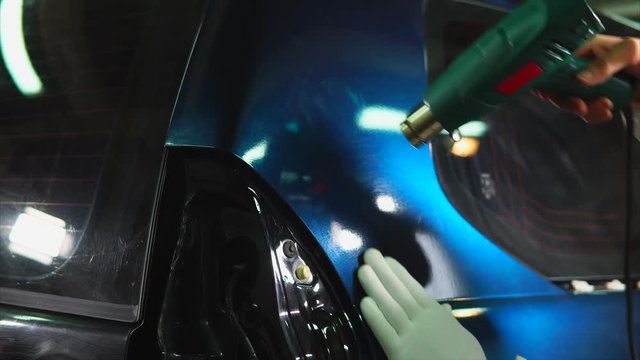Man working in the showroom applied vinyl on the machine, using a carboxylic film. Master uses a hairdryer to dry the film and better adhesion to the car.