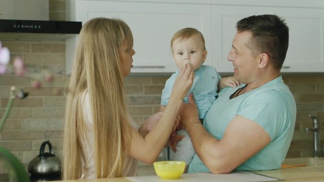 Young parents play with their little son, they try to feed him from a spoon