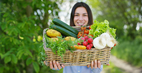 Beautiful young girl holding a basket of vegetables, in the background of nature. Concept: biology,...