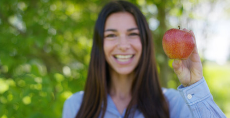 Beautiful young girl holds in hands a fresh ripe red apple, in the background of nature. Concepts: biology, bio products, bio ecology, growing fruit, diet, natural clean and fresh product, environment