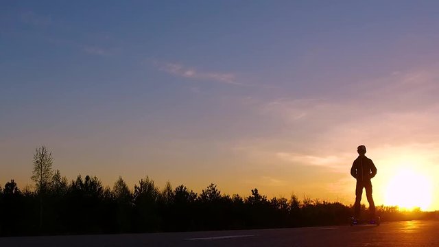 Teenager on the segway rides from the sunset. Silhouette. Slow Mo.