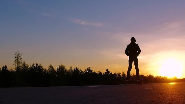 A guy on a hoverboard ride towards sunset. Silhouette. SlowMo.