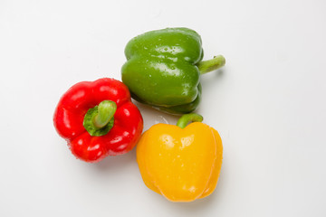 Three bulgarian peppers of different colors lie in a row on a white background. View from above.