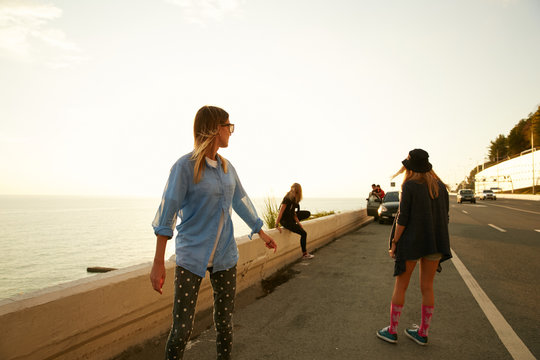 Girls travelers walking down the roadside on the sea coast on the sunset