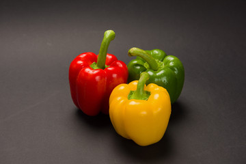 Three bulgarian peppers of different colors lie in a row on a black background.