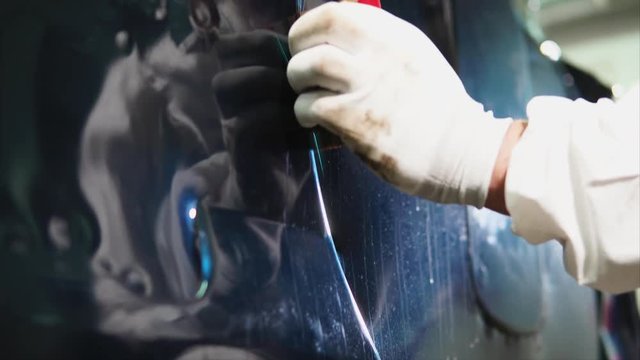 Close up shot of man applying vinyl film while tuning expensive blue car.
