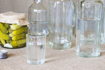 Crystal glass and bottle and pickled cucumber on a sacking background.