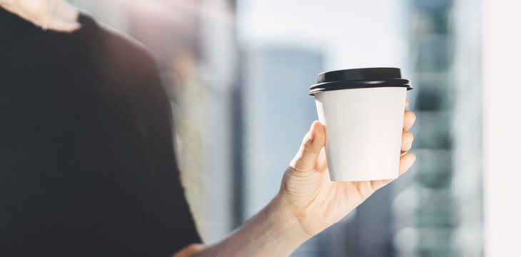 Close Up Of Female Hand Holding Paper Cup Of Coffee Outdoor, Hipster Woman Enjoying Coffee To Go, Mock-up Of White Cup Of Coffee In Female Hand In Sunny Park