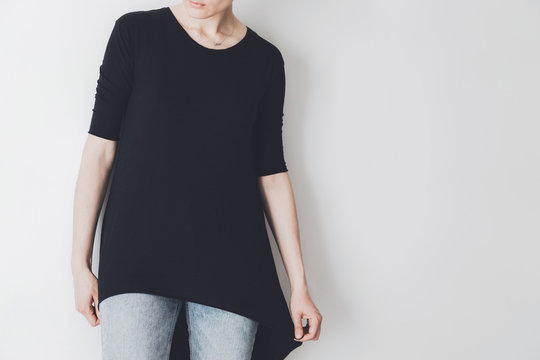 Young hipster girl wearing black oversize t-shirt with blank space for your logo or design, mock-up of black cotton t-shirt, white wall in the background