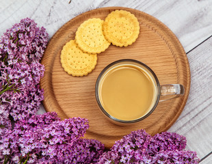Fototapeta na wymiar glass coffee Cup with cookies and milk on a background of purple lilac on a wooden stand