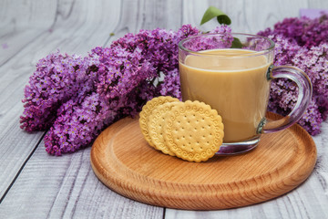Fototapeta na wymiar glass coffee Cup with cookies and milk on a background of purple lilac on a wooden stand