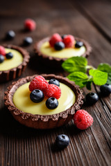 Cocoa tartlets filled with vanilla pudding and topped with blueberry and raspberry