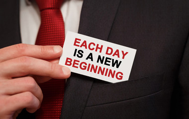 Businessman putting a card with text Each day is a new beginning in the pocket