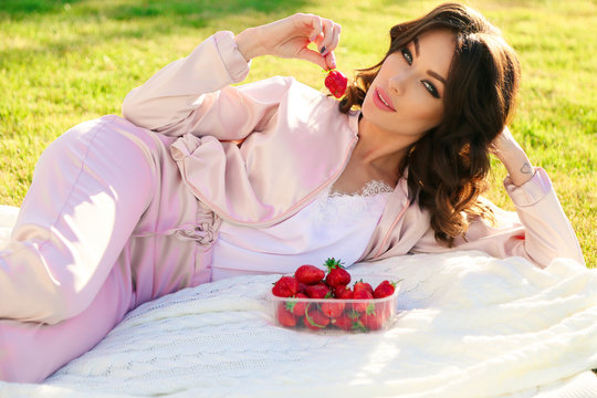 beautiful girl with dark hair relaxing at summer picknic, eating strawberries