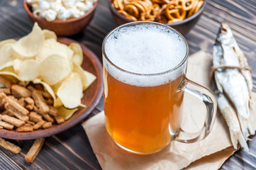 Lager beer mug and snacks on wooden table. Nuts, chips, crackers and dry fish