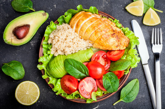 Healthy dinner with quinoa, chicken, tomatoes, avocado, spinach and lettuce leaves.  Buddha bowl. Healthy salad bowl on dark background. Top view