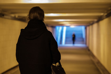 A girl in black clothes is walking along an underground passage.