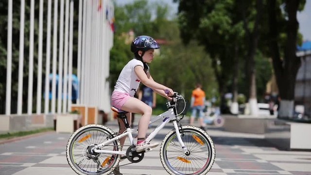 Happy little girl riding a bicycle in the city park at summer sunshine day.