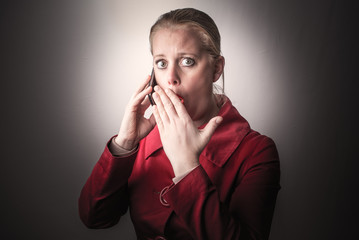 Speaking on phone shocked girl covers her mouth with hand, isolated on grey