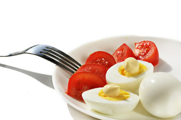 Chicken boiled eggs on a white plate with slices of red tomato on a white background