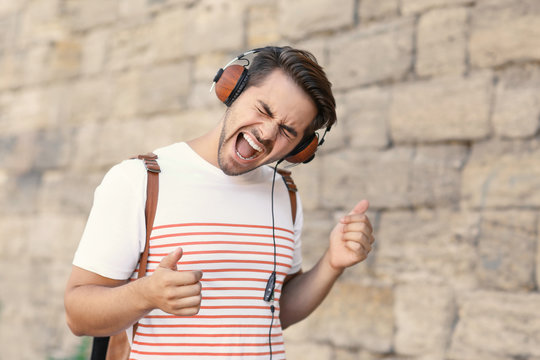 Handsome man with headphones listening music on brick wall background
