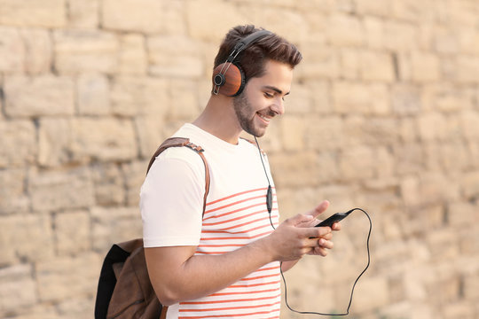Handsome man with headphones listening music on brick wall background