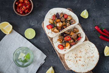 Fototapeta na wymiar Tacos with grilled mushrooms, Spanish spicy sausage chorizo, Mexican tortillas, Cypriot cheese halloumi, hot chilly, dried oregano and glass of water with lime, top view on dark rustic background