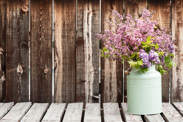 Large bouquet of lilacs in a green container on a rustic wooden table.