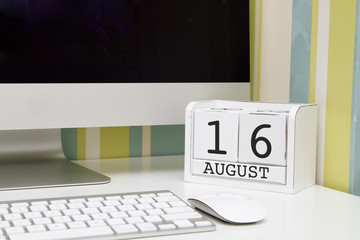 Cube shape calendar for AUGUST 16 and computer with white screen on table. 