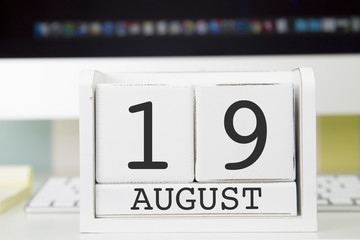 Cube shape calendar for AUGUST 19 and computer with white screen on table. 