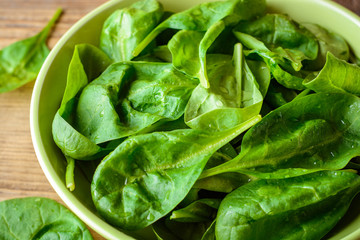 Washed fresh spinach leaves in bowl on rustic wooden table.
