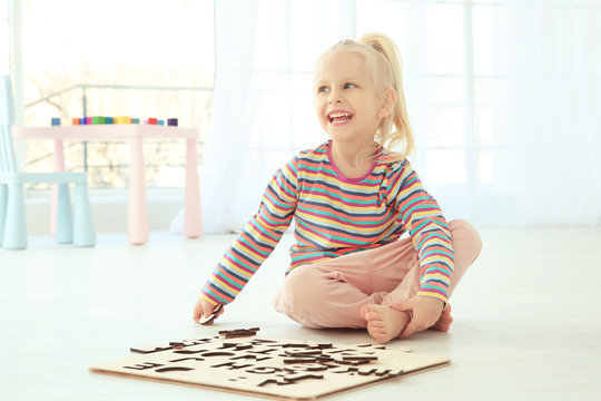 Cute little girl playing with letters while sitting on floor at home