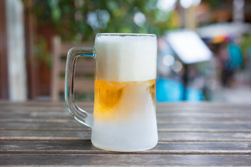 The Frozen mug of cold light beer in the pub on wood table, close up