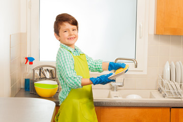 Boy in rubber gloves washing plates with sponge