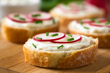 Bread slices with cream cheese, radish slices and chives on wooden board, photographed with natural...