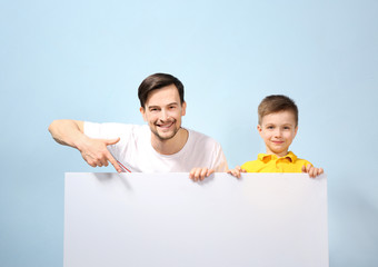 Handsome man and his son with poster on color background