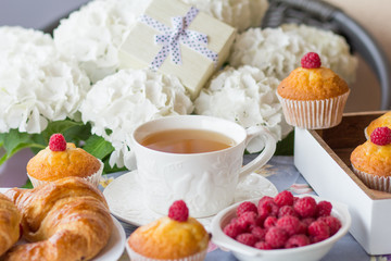 A festive morning breakfast, tea with croissants, muffins and raspberries on a background of white flowers