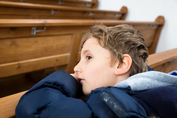 young boy child sitting in a church on the pew, look and think