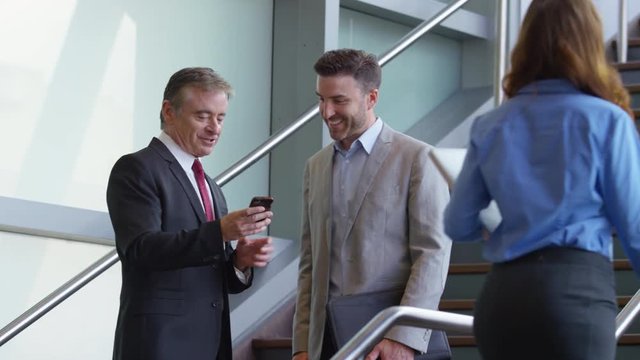 Two businessmen meeting on stairs of office lobby looking at cell phone