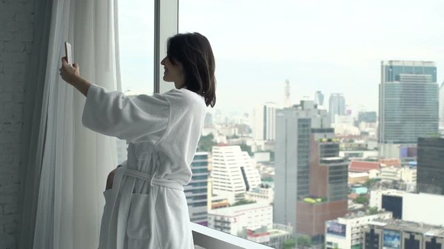 Happy woman taking selfie photo with cellphone by window at home, super slow motion 120fps
