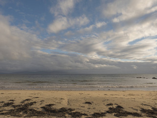 Clouds over ocean and sandy beach with sea weed,