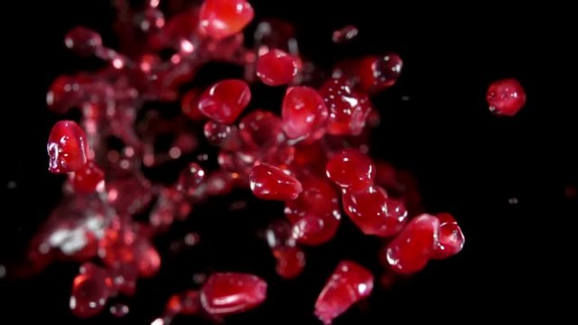 Red ripe garnet grains with juice fly to the camera on a black background in slow motion