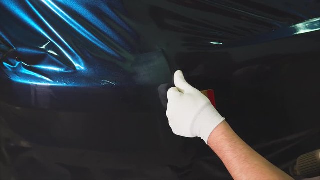 Man working in the showroom applied vinyl on the machine, using a carboxylic film. Master uses a hairdryer to dry the film and better adhesion to the car.