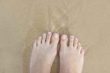 Female feet in the sand. There is a wave, and I stand and wait. Copy space. From top to bottom.